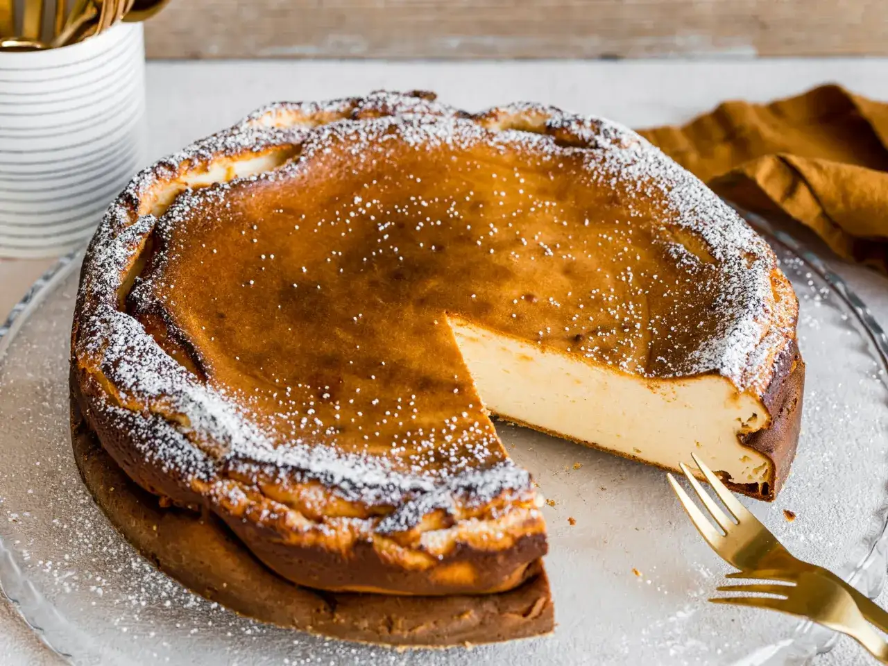 Ein köstlicher Quarkkuchen ohne Boden, mit Puderzucker bestäubt, wartet auf seine Verkostung. Ein Stück ist bereits angeschnitten.