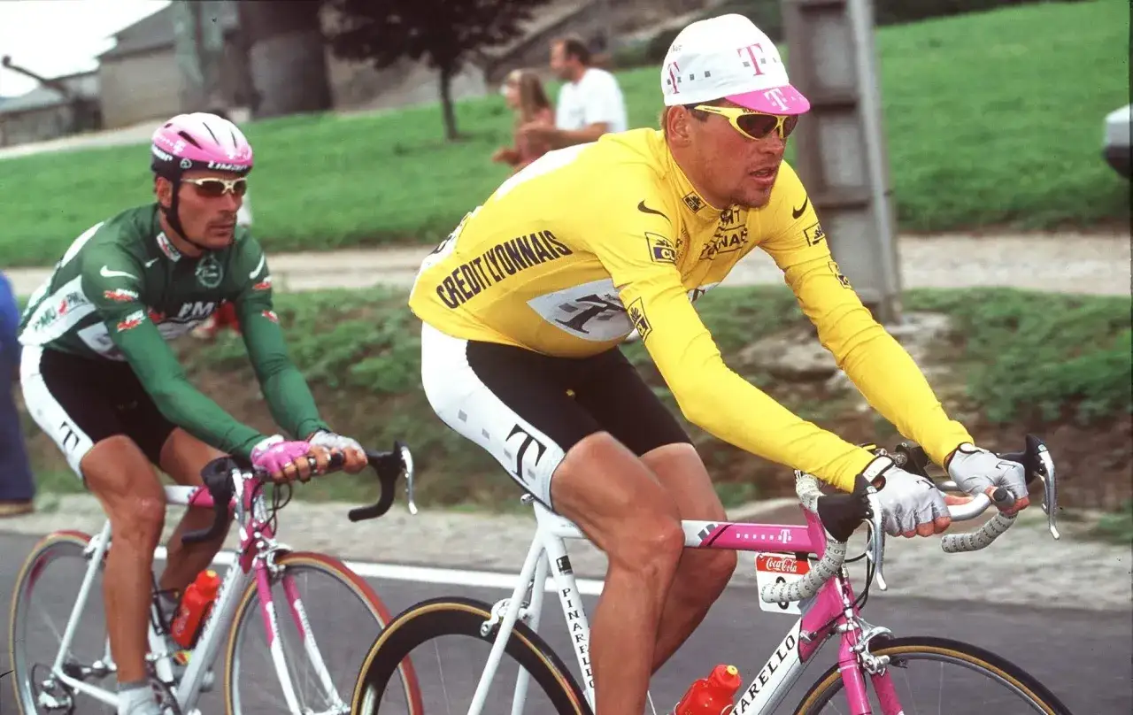 Jan Ullrich 1997 im gelben Trikot, auf dem Weg zum Sieg. Ein Radfahrer in Grün folgt ihm dicht auf den Fersen.