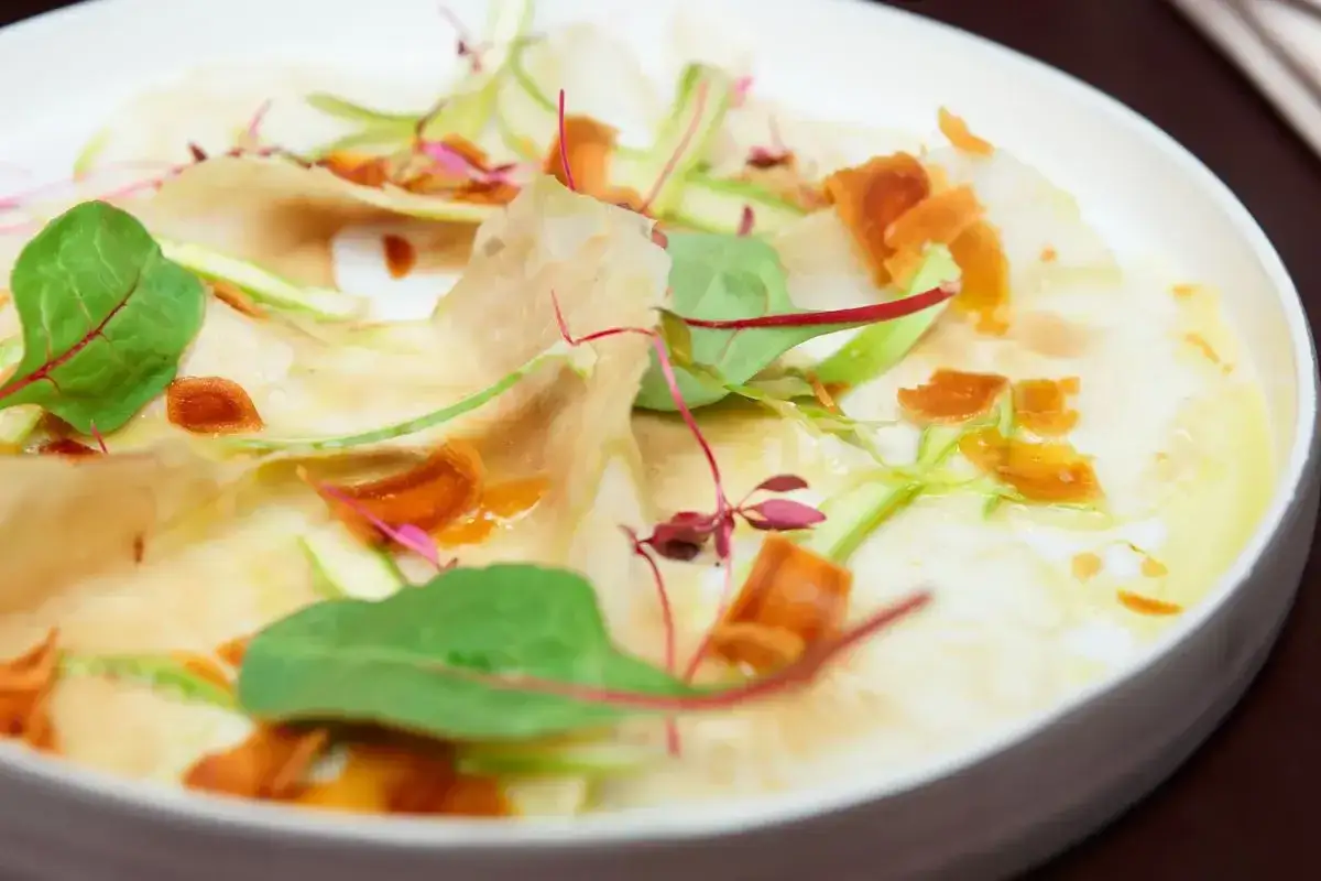 Carpaccio di sedano rapa crudo, sottili fette con germogli verdi e croccanti sfoglie arancioni. Un'idea fresca per le tue ricette.