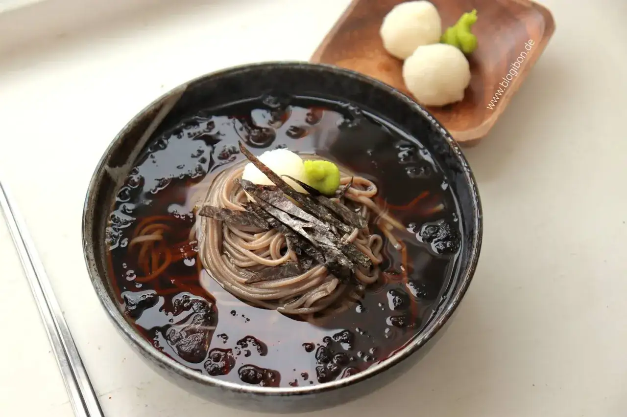 Sch&uuml;ssel mit Mul Naengmyeon, kalter Buchweizennudelsuppe, garniert mit Algen und Wasabi. Daneben kleine Reisb&auml;llchen.