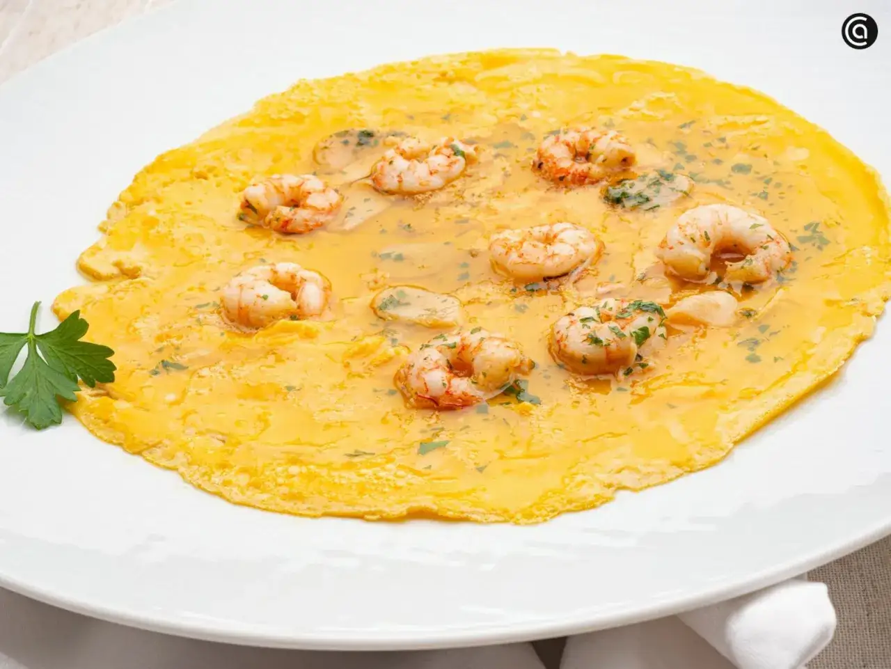 Tortilla de gambas jugosa y dorada, con gambas enteras y perejil picado, servida en un plato blanco.