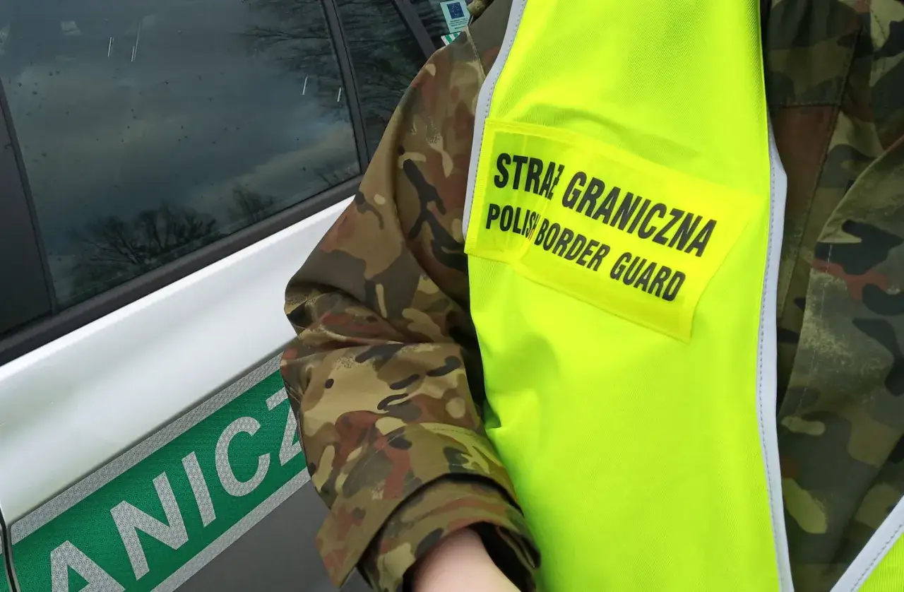 Funkcjonariusz Straży Granicznej w kamizelce odblaskowej obok oznakowanego pojazdu, przygotowany do akcji, być może związanej z deportacją.