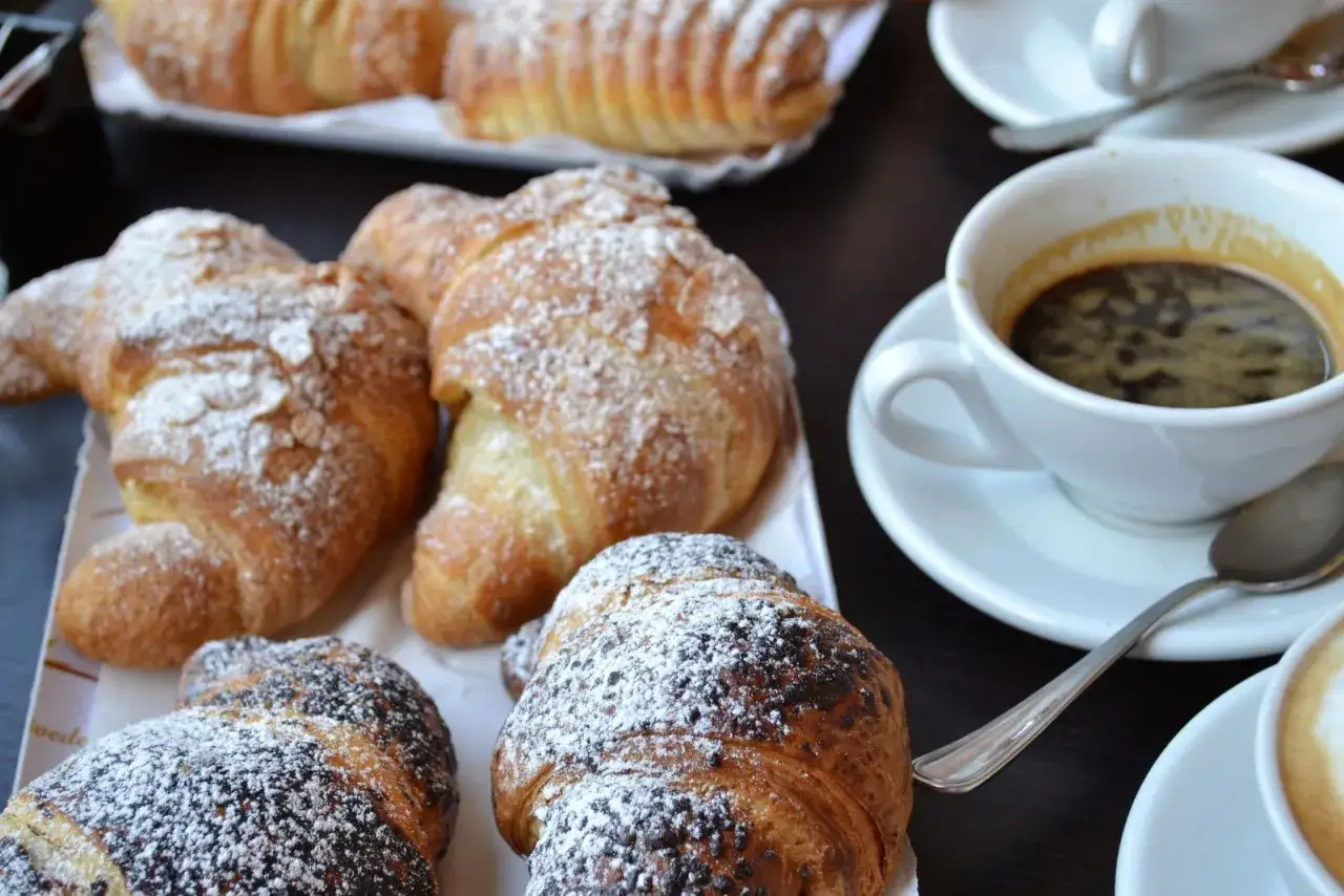 Un délicieux petit déjeuner italien : croissants saupoudrés de sucre glace et de chocolat, accompagnés de tasses d'espresso fumant.