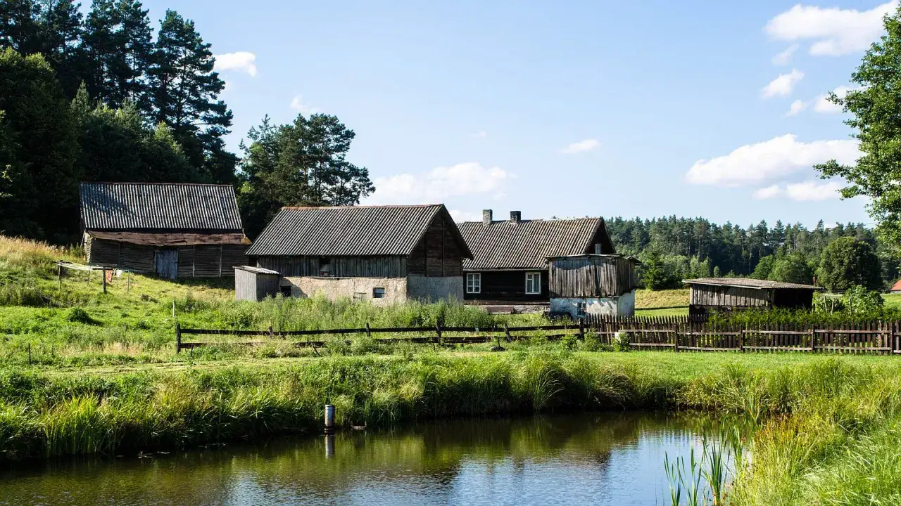 Nietypowe atrakcje Mazury: malownicza wieś z drewnianymi domami i stawem, otoczona zielenią i lasem.