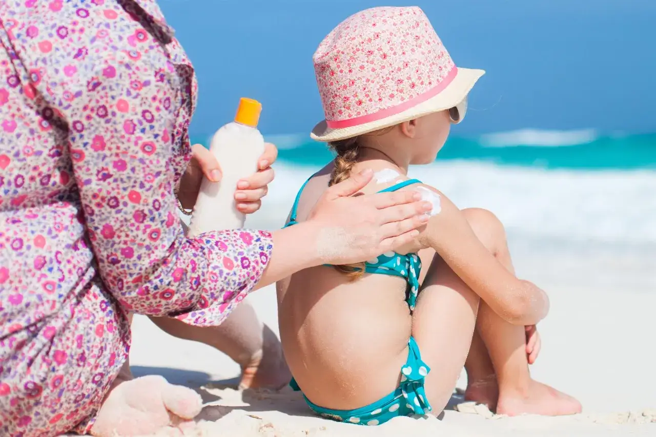 Mamma applica la crema solare a una bambina sulla spiaggia, per prevenire la dermatite da sabbia.