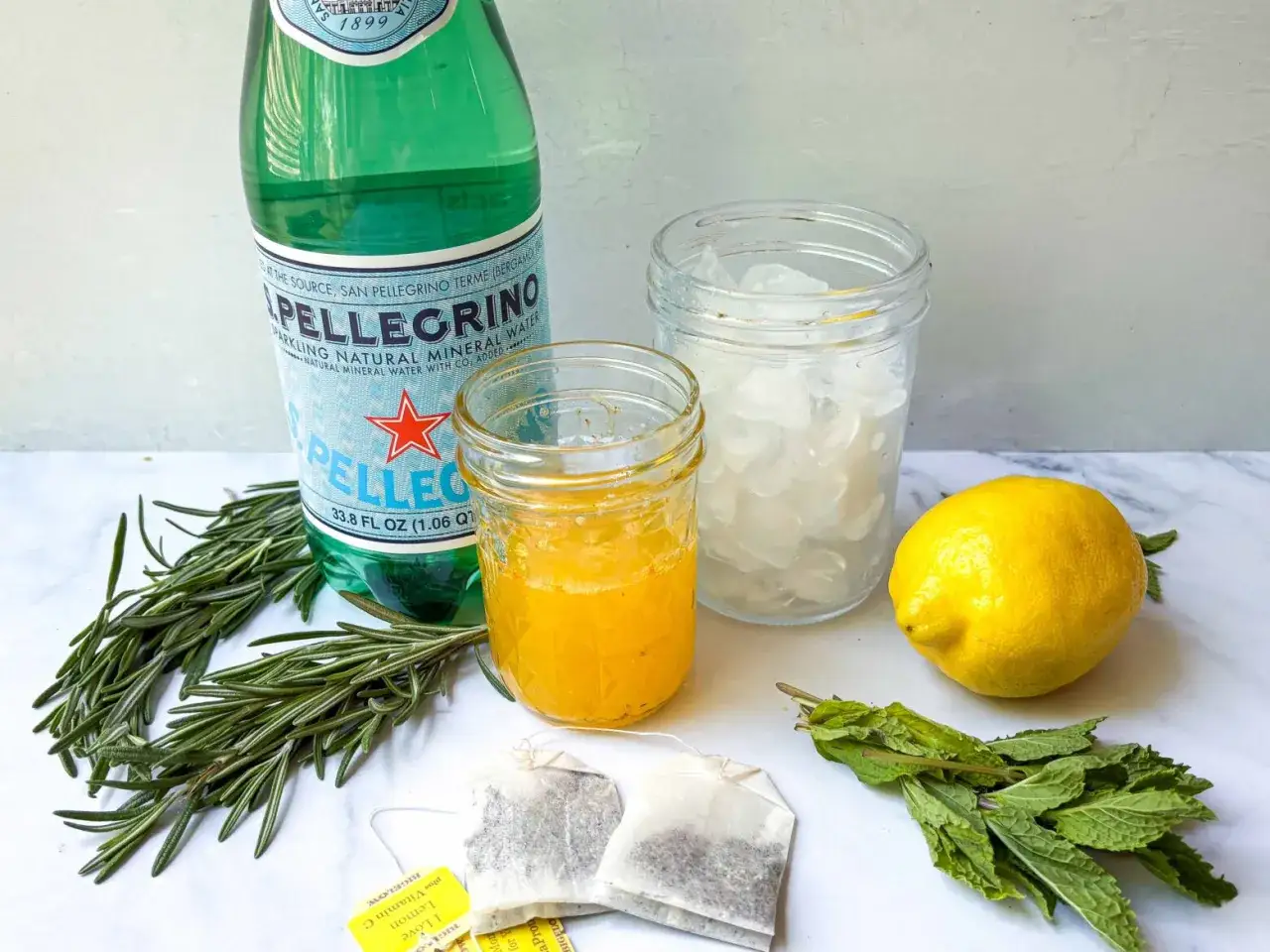 Ingredienser för ett uppfriskande citronmeliss recept: S.Pellegrino, citron, mynta, rosmarin, is och te.