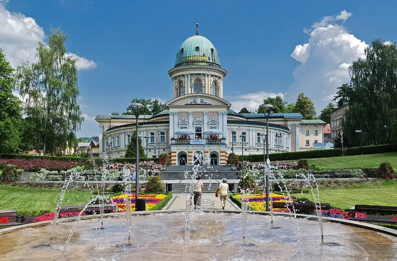 Piękny park z fontanną i kwitnącymi rabatami kwiatowymi przed zabytkowym budynkiem. Lądek Zdrój atrakcje zachwycają.