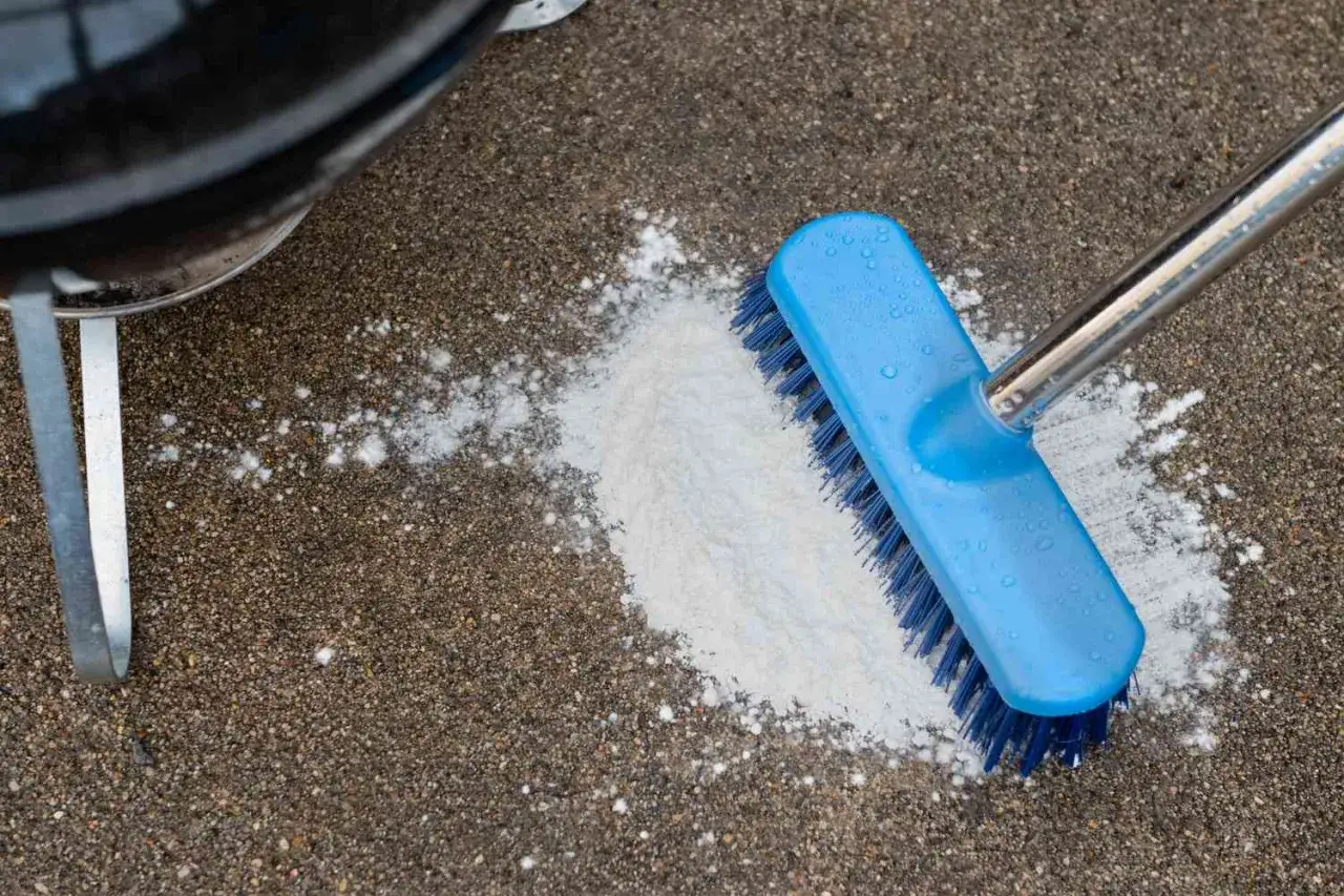 A blue brush is used to scrub a pile of white powder on a concrete patio, demonstrating how to clean concrete patio.