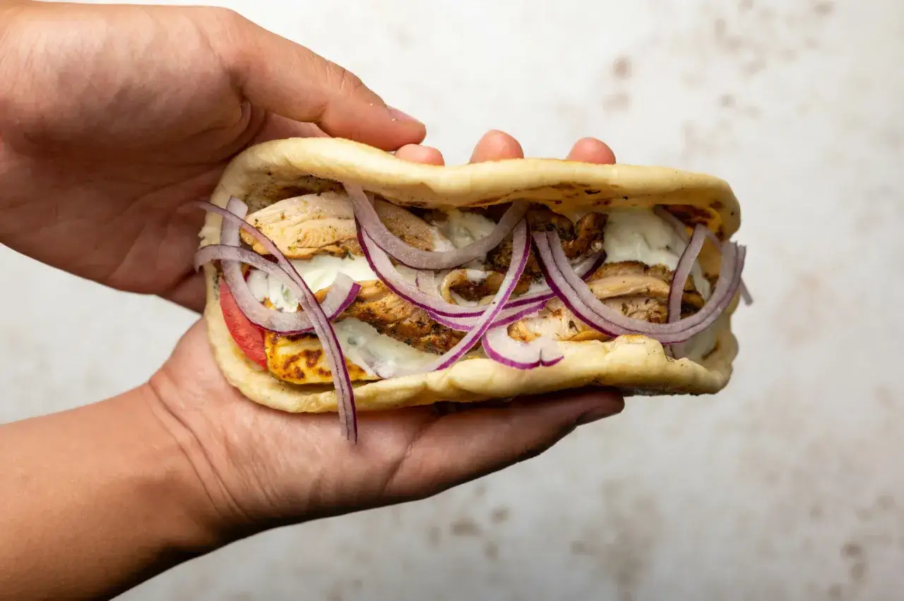 Ein saftiges Pita Brot gefüllt mit Hähnchen, Tomaten, Zwiebeln und Joghurt-Dressing, gehalten in einer Hand.