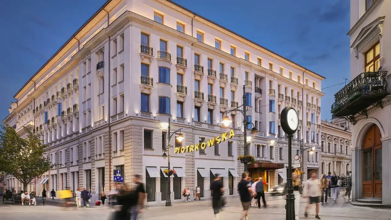Elegancki hotel B&B Łódź przy ulicy Piotrkowskiej. Budynek z balkonami i ozdobnymi detalami, oświetlony wieczorem.