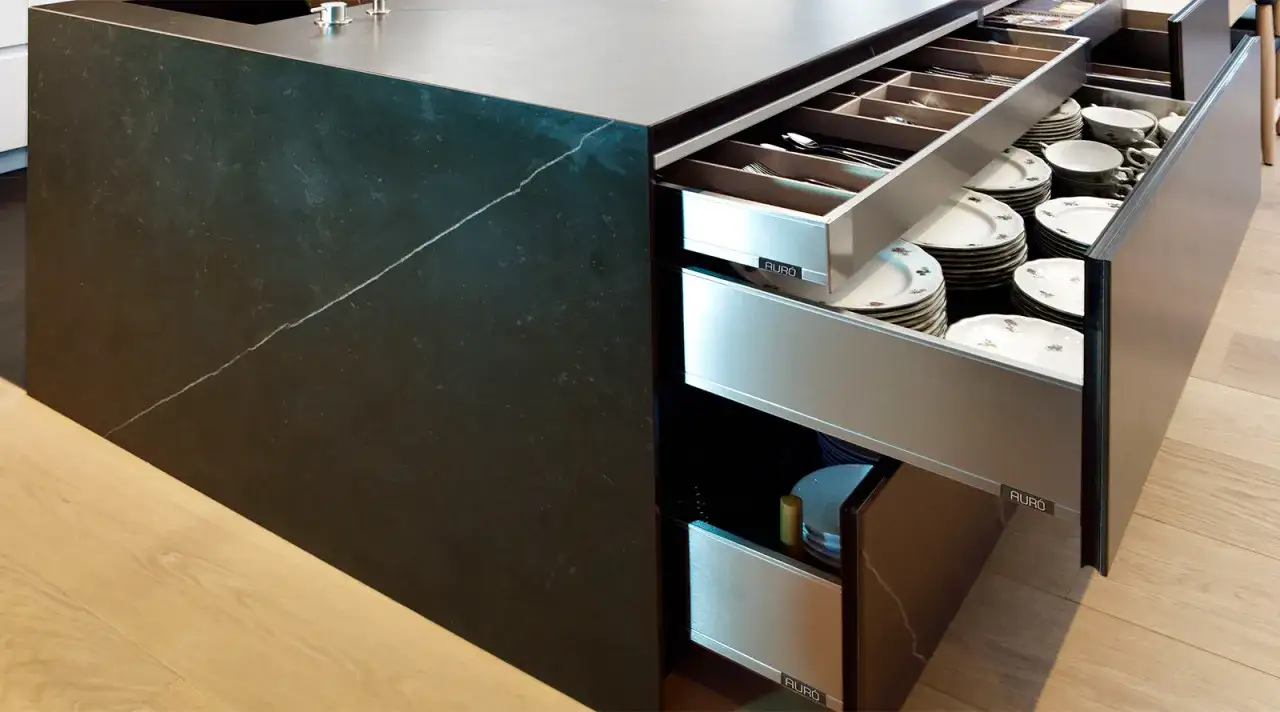 Encimera de cocina de porcelana negra con vetas blancas, mostrando cajones organizados con vajilla y cuberter&iacute;a.