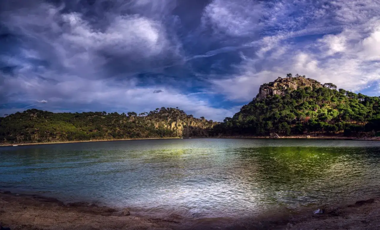 Agua serena en la playa virgen de la nueva, rodeada de colinas boscosas y un cielo dramático.