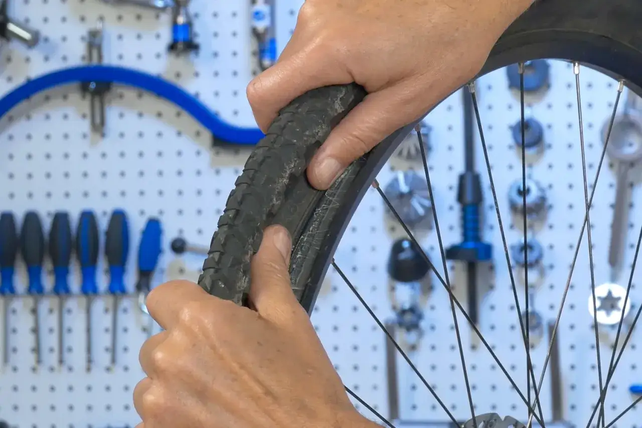 H&auml;nde montieren einen tubeless reifen. Werkzeuge h&auml;ngen an der Wand im Hintergrund.