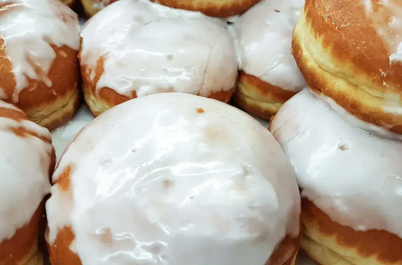 Pyszne pączki z białym lukrem, gotowe do jedzenia. Idealny lukier do pączków sprawia, że są jeszcze smaczniejsze.