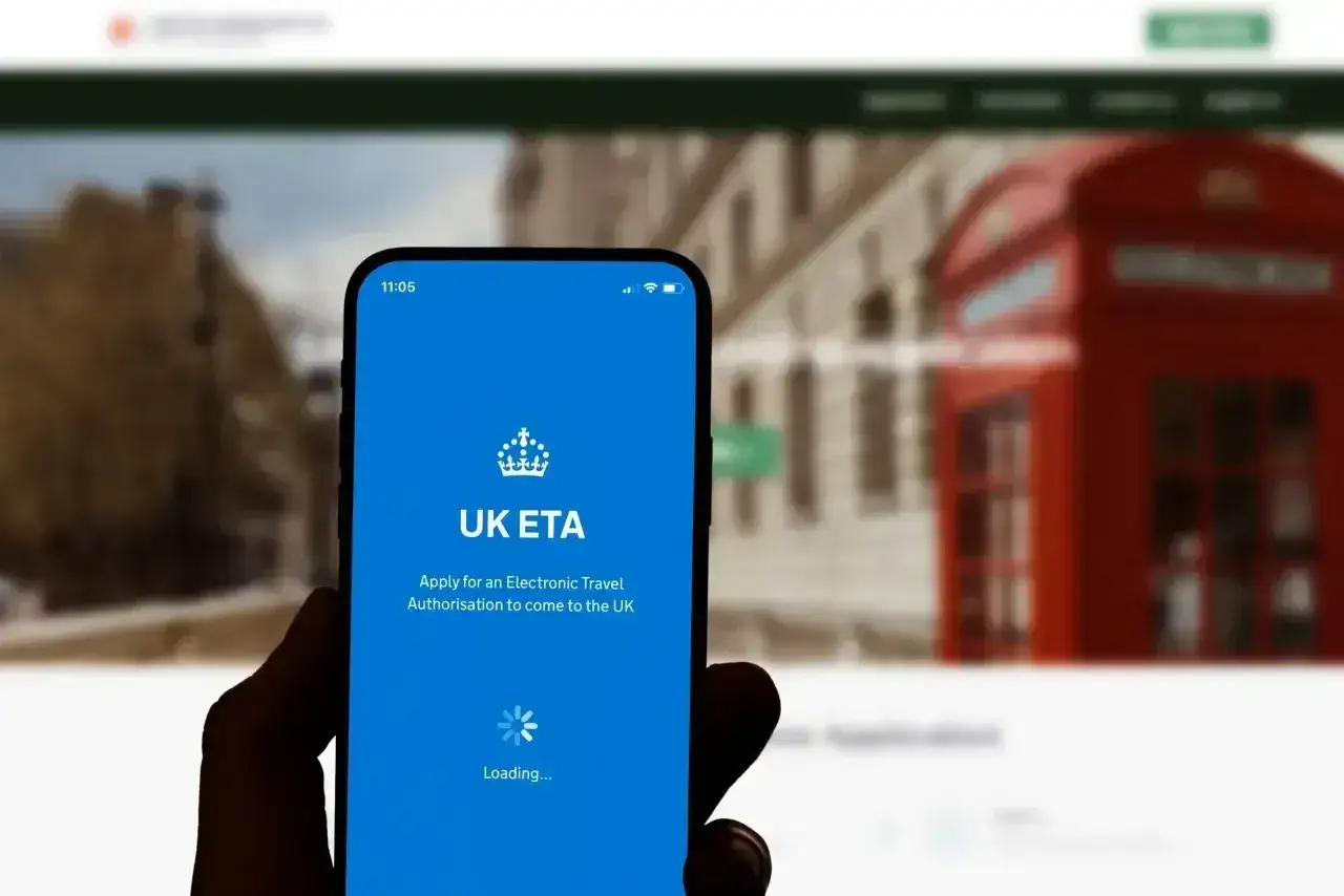 Telefon z aplikacją UK ETA, która ułatwia uzyskanie wizy do Anglii. W tle londyńska budka telefoniczna.