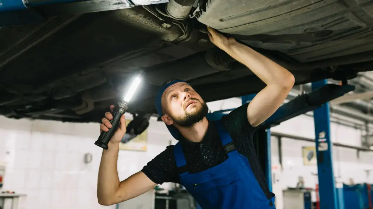 Mechanik z latarką bada podwozie auta, szukając przyczyny problemu ze zmianą bieg&oacute;w.