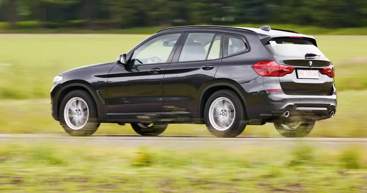 Czarne BMW X3 w ruchu, na tle zielonych pól. Zastanawiasz się, ile kosztuje BMW X3? Ten model wygląda na dobrze wyposażony.