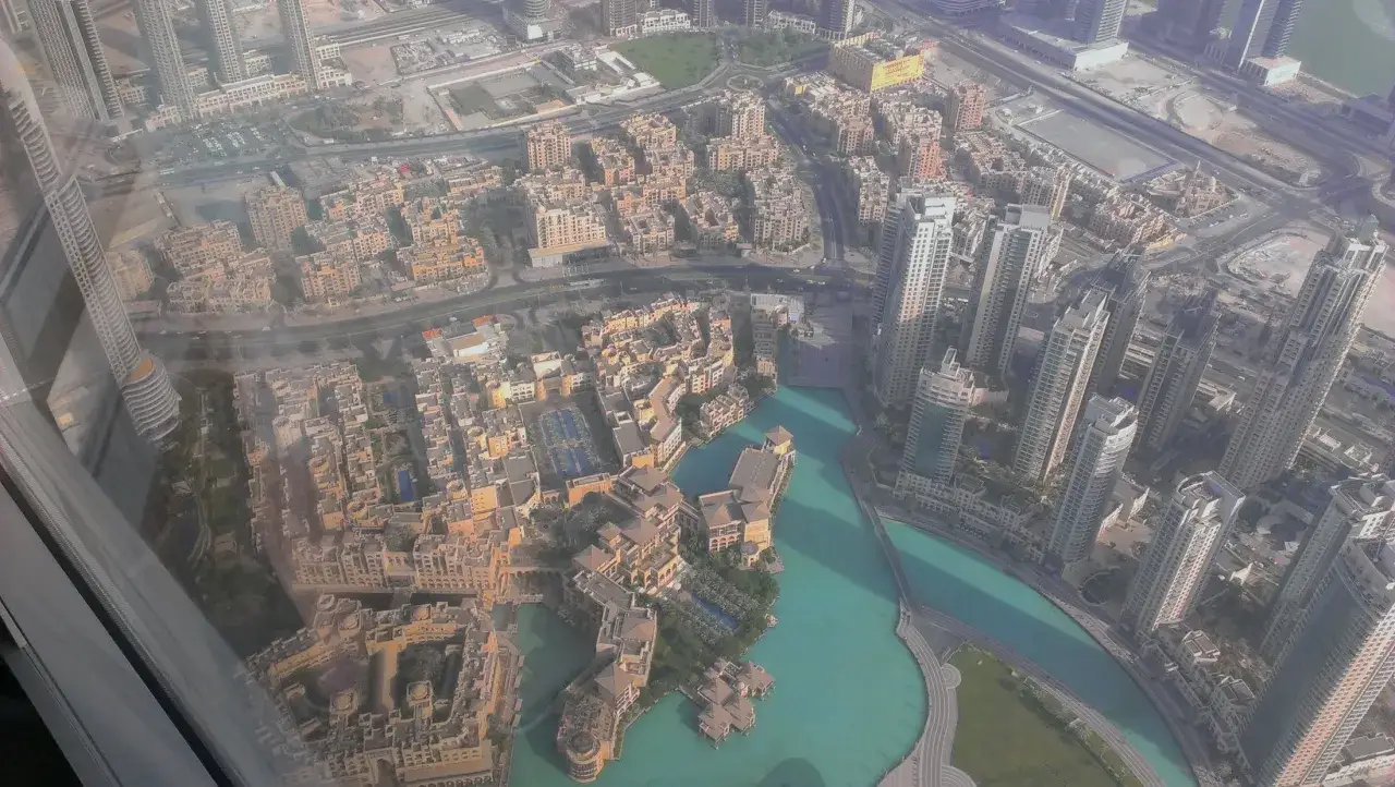 Widok z góry na Dubaj, gdzie jest Burj Khalifa. Widać nowoczesne wieżowce, zabudowania mieszkalne i turkusową wodę.