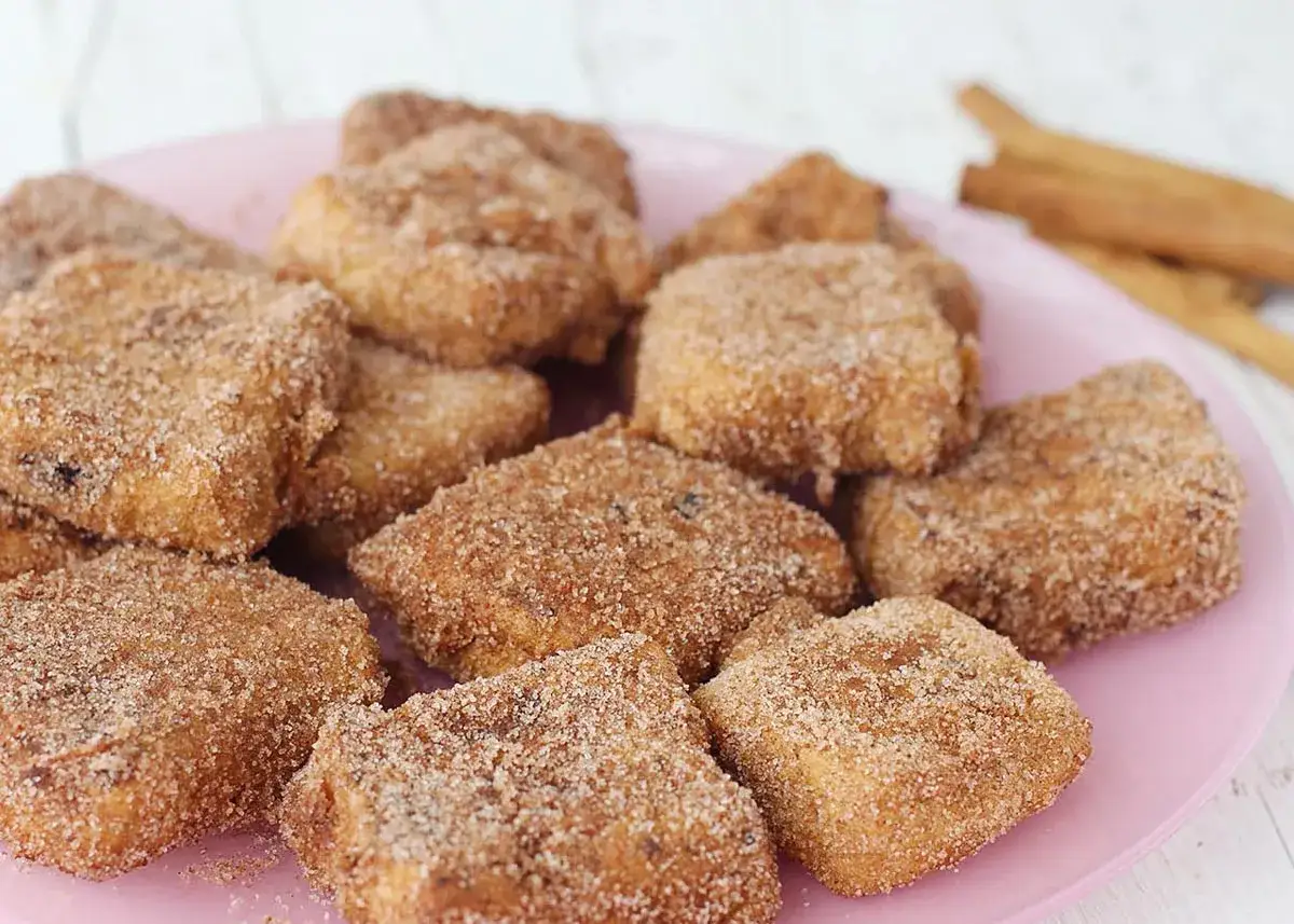 Deliciosa leche frita Thermomix, rebozada en az&uacute;car y canela, servida en un plato rosa.