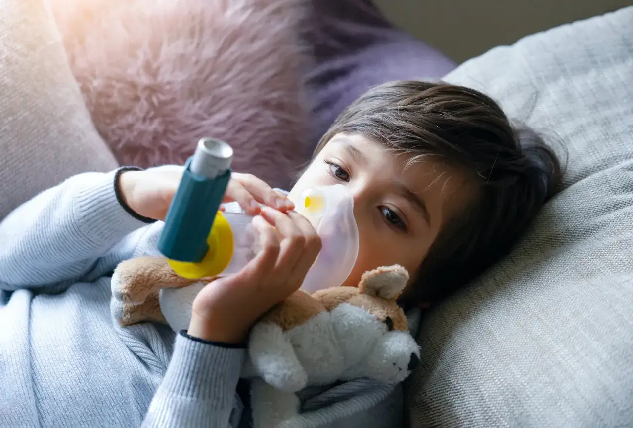Bambino con maschera e inalatore per gestire il broncospasmo. Un peluche lo conforta.