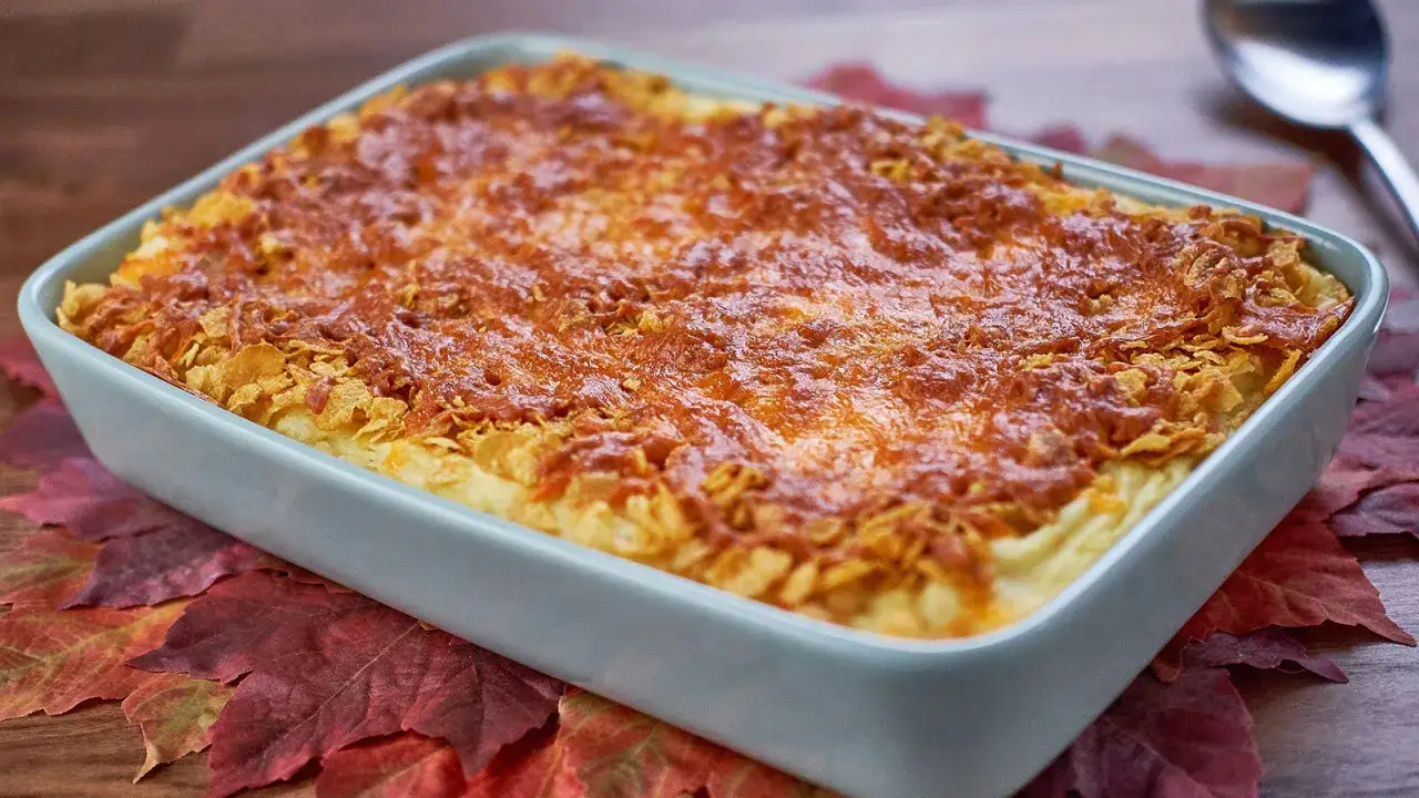 Pastel de patata gratinado con queso y cereales crujientes, servido sobre hojas de oto&ntilde;o.