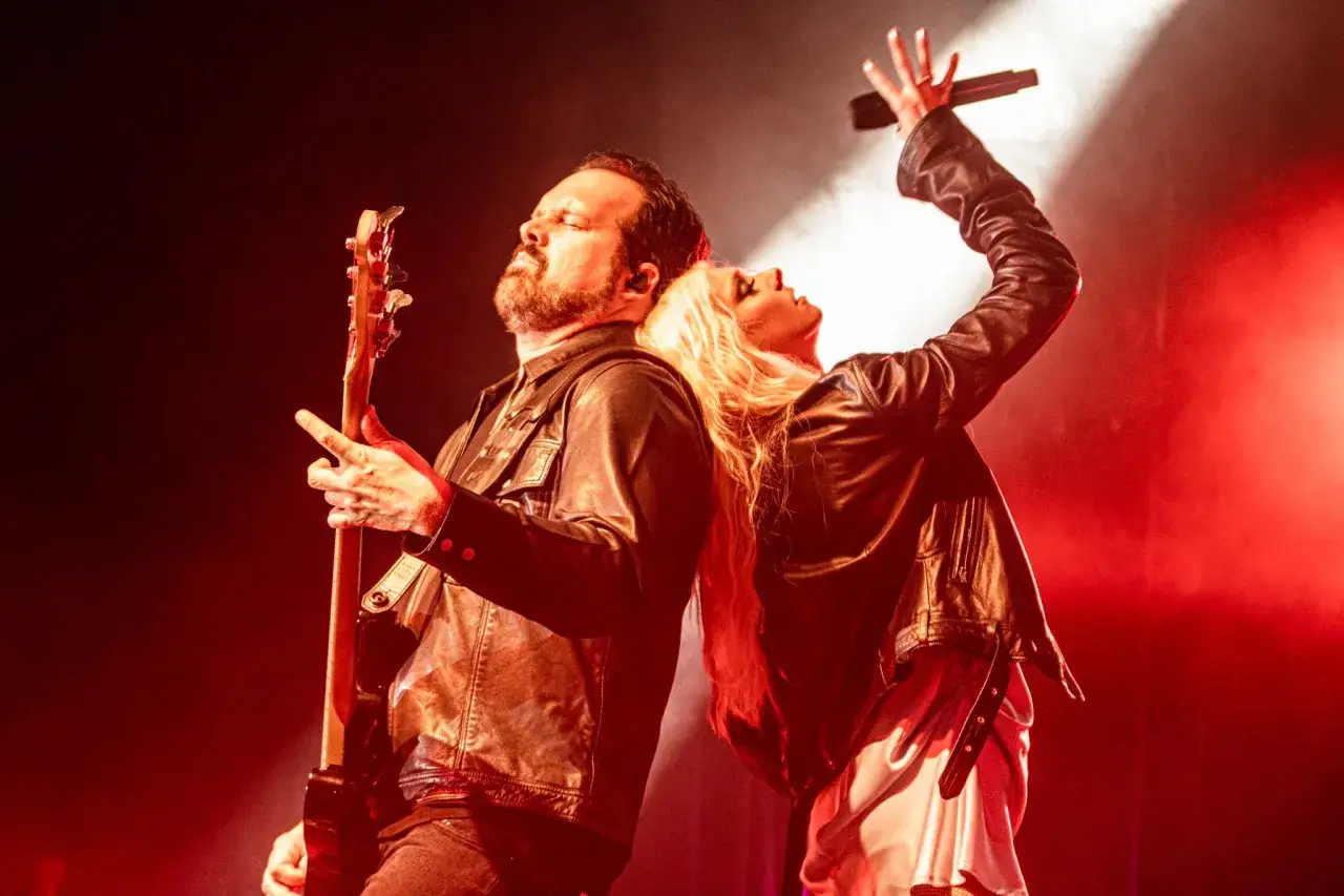Les membres de The Pretty Reckless, un homme jouant de la guitare et une femme chantant, dos &agrave; dos sur sc&egrave;ne sous des lumi&egrave;res rouges.