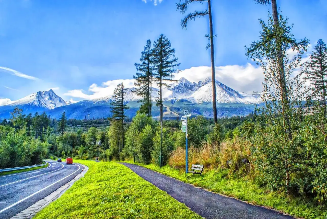 Droga wije się wśród zieleni, a w oddali majaczą ośnieżone szczyty Tatr. Idealne miejsce na **velo Tatry** i podziwianie krajobrazów.