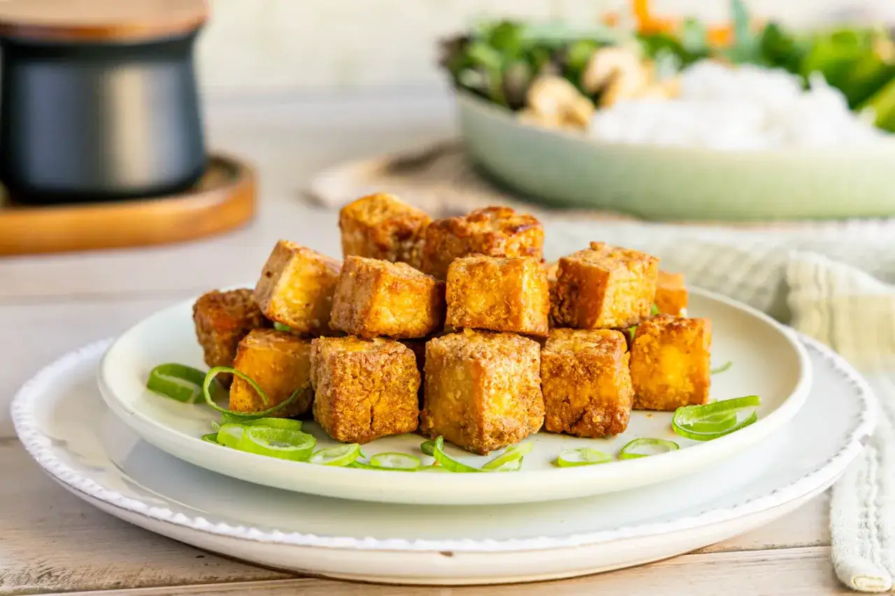 Goldbraun gebratene Tofuwürfel, perfekt zum tofu zubereiten, garniert mit Frühlingszwiebelringen auf einem Teller.