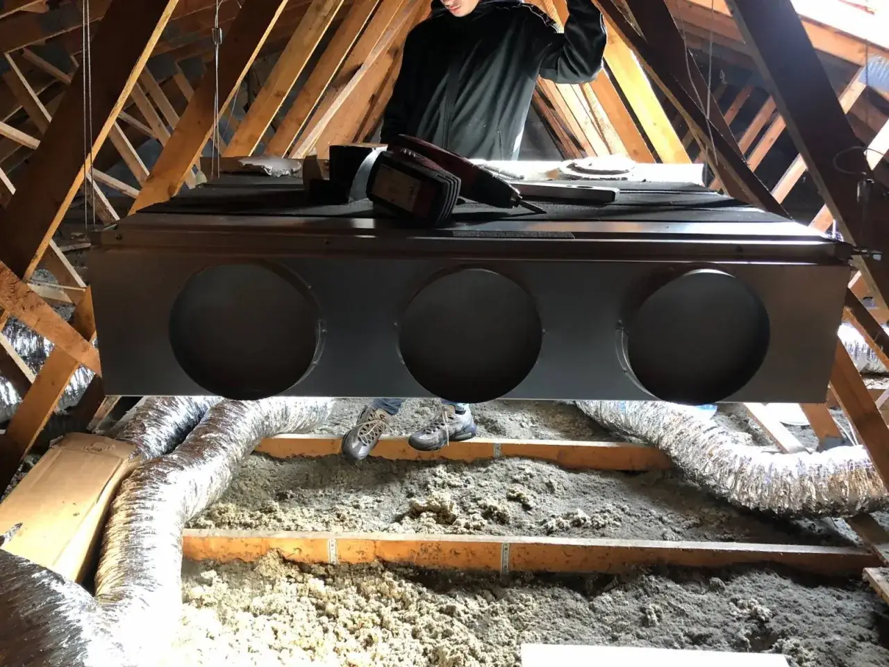 Installation d'un syst&egrave;me de climatisation gainable dans un grenier. Un technicien est visible, pr&ecirc;t pour l'entretien.