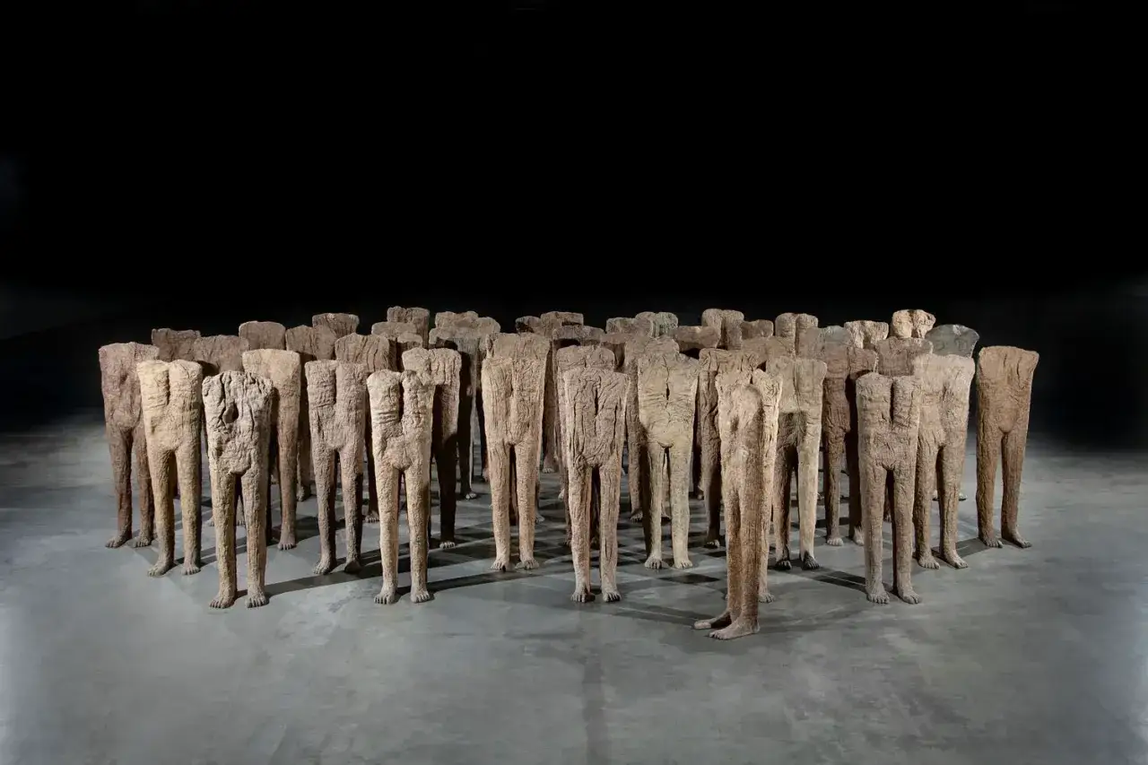 Grupa bezgłowych postaci, dzieło Magdaleny Abakanowicz, stoi w milczącym tłumie.