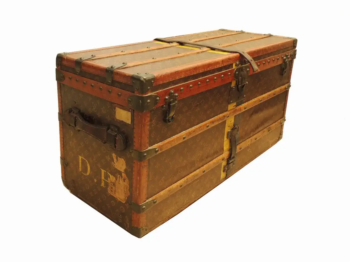 Baule vintage Louis Vuitton, simbolo del fondatore. Dettagli in pelle e metallo, monogramma iconico.