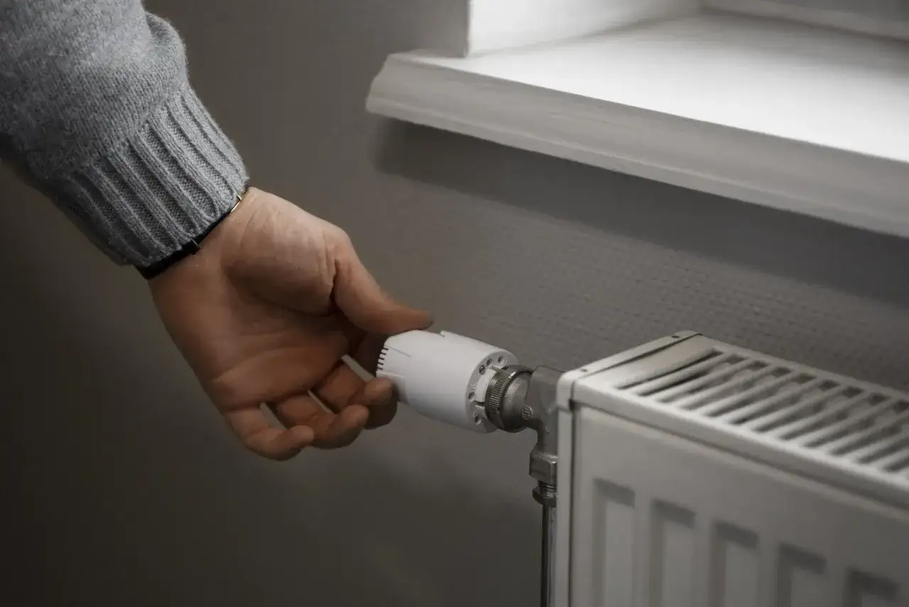 Dłoń reguluje termostat grzejnika. Zastanawiasz się, ile kosztuje wymiana grzejnika?