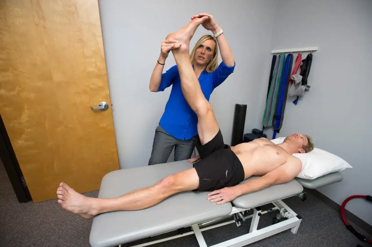 Fisioterapista assiste uomo in esercizi di stretching per il piede e la gamba, sdraiato su un lettino.