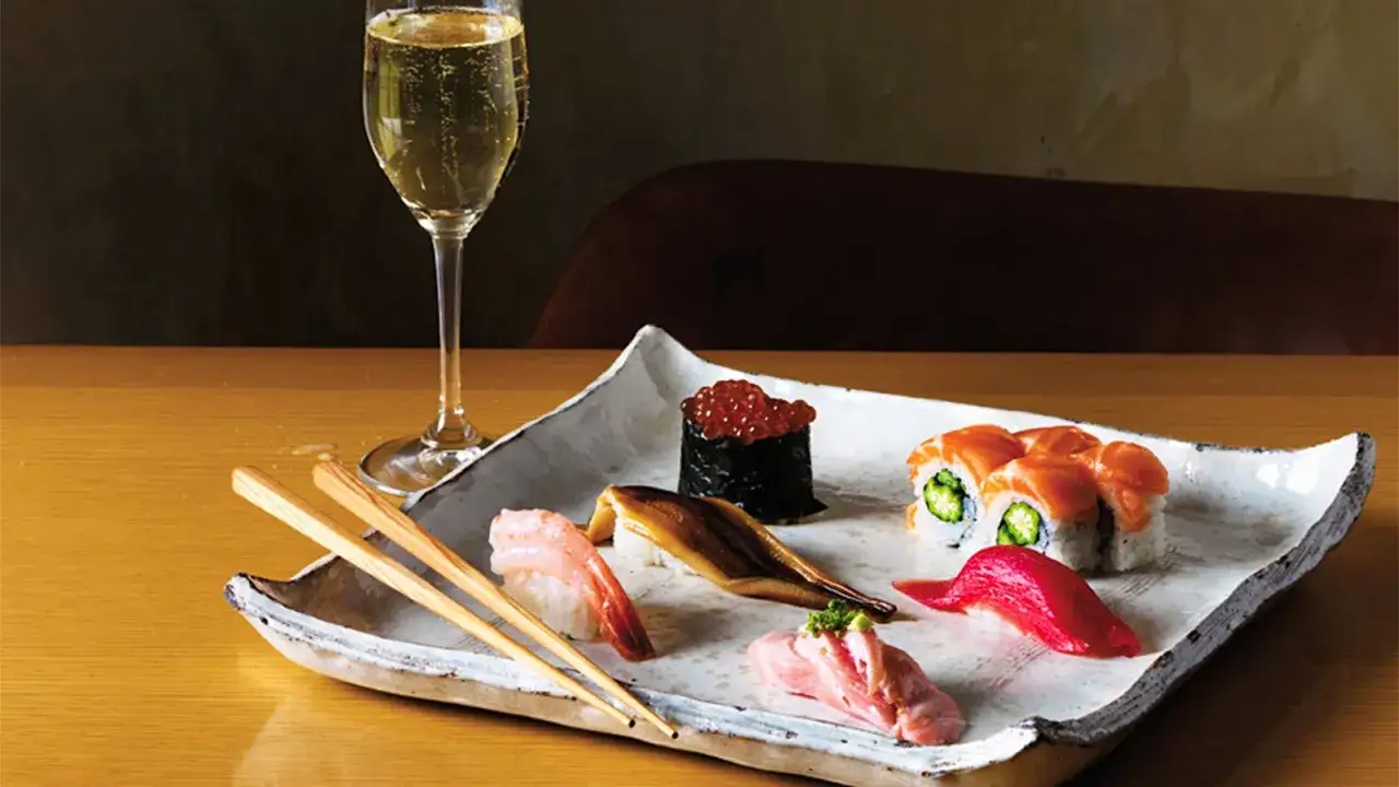 En elegant tallrik med olika sorters sushi, inklusive lax, räka och ål, serveras med ett glas bubbel. Perfekt vin till sushi.