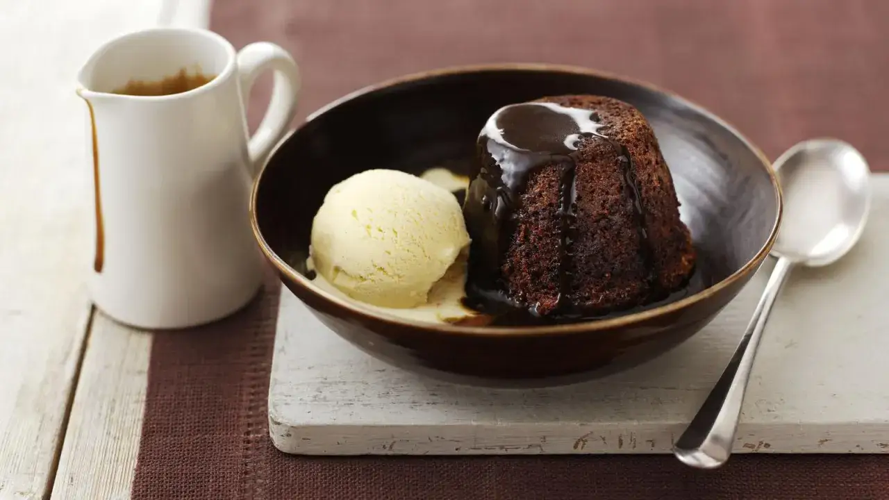 En läcker chokladpudding med vaniljglass, perfekt för ett sticky toffee pudding recept. En kanna med sås står bredvid.