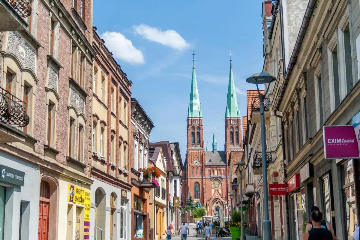 Ulica w Rybniku z widokiem na kości&oacute;ł, pełna sklep&oacute;w i kawiarni. To świetne miejsce na spacer i odkrywanie lokalnych atrakcji.