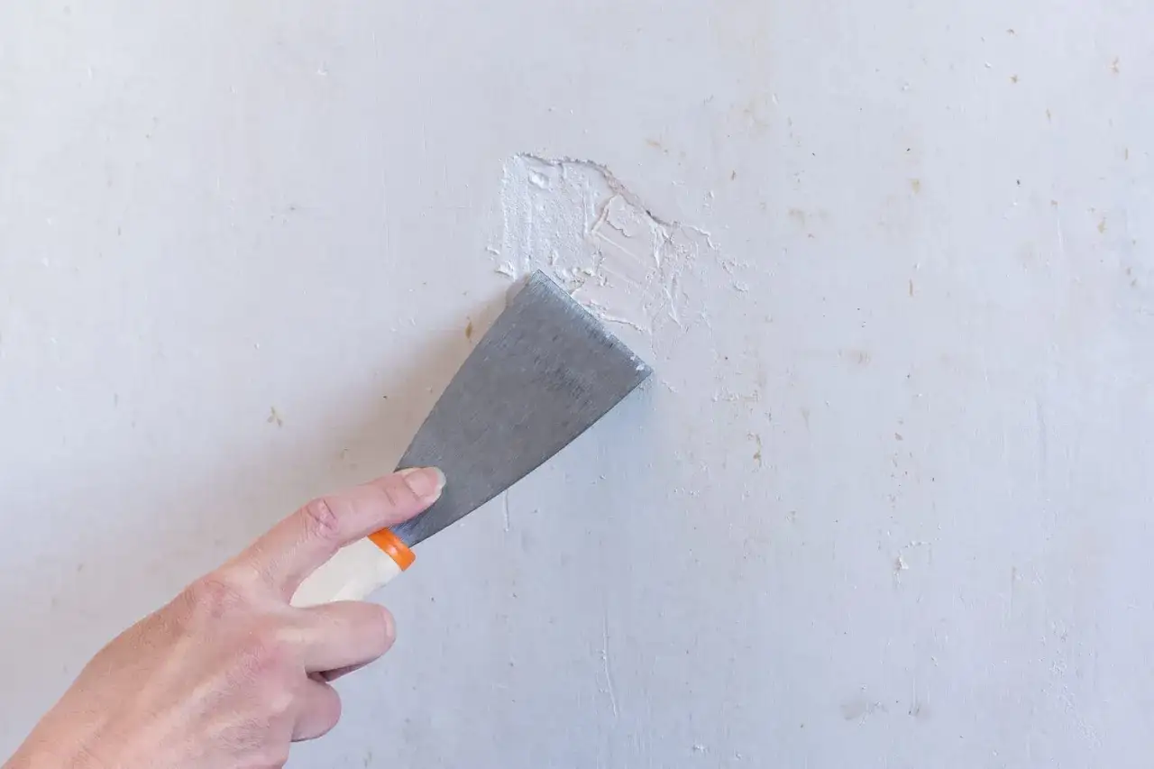 Main tenant utilise un couteau à mastic pour appliquer du plâtre ou enduit de rebouchage sur un mur abîmé.