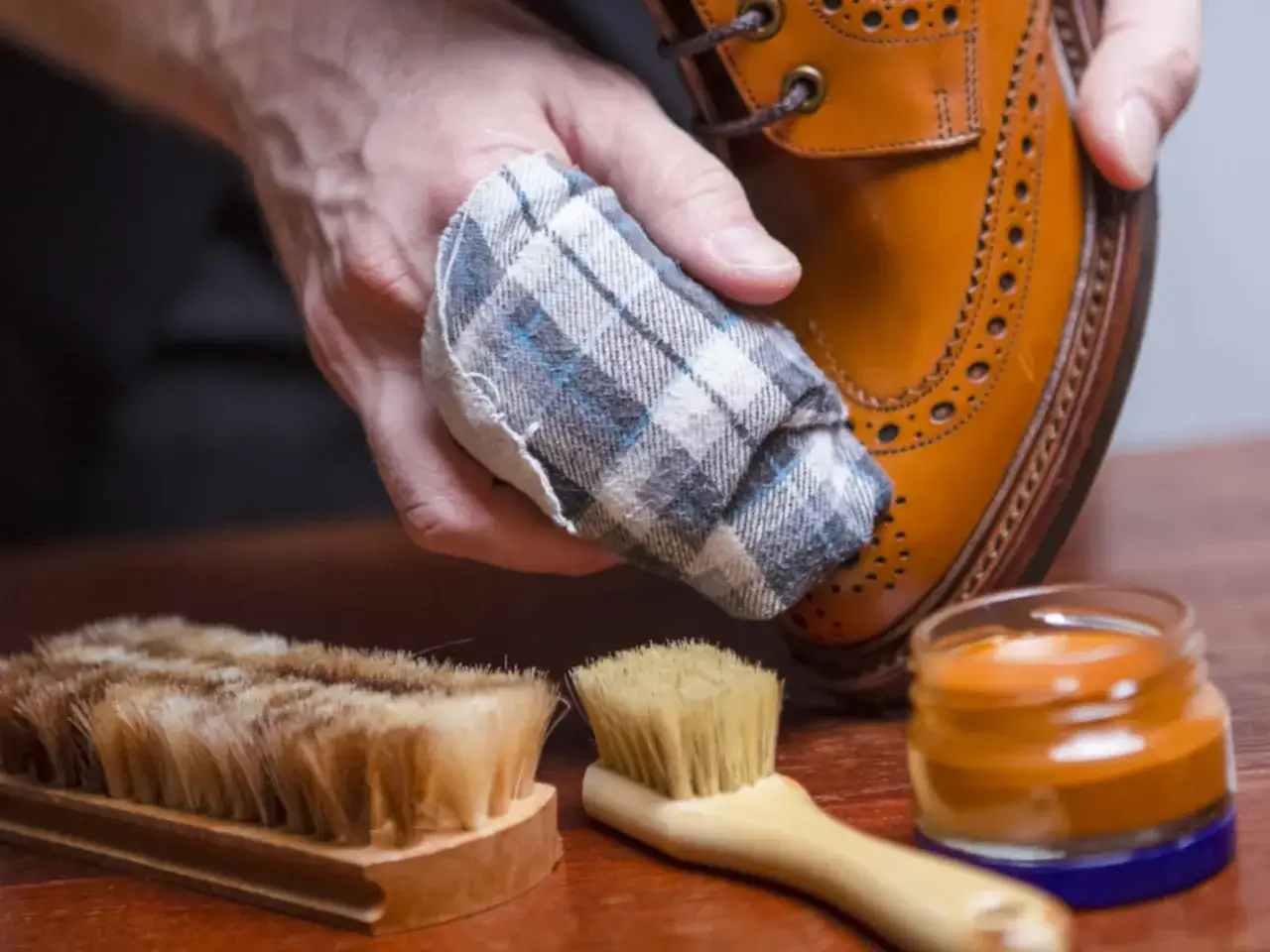 C&oacute;mo limpiar zapatos de piel: mano con pa&ntilde;o puliendo zapato, cepillos y crema para calzado.
