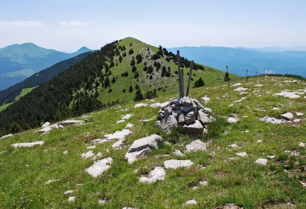 Cumbre rocosa con un mojón de piedras y postes de madera. El paisaje montañoso de la costa pubilla se extiende hasta el horizonte.