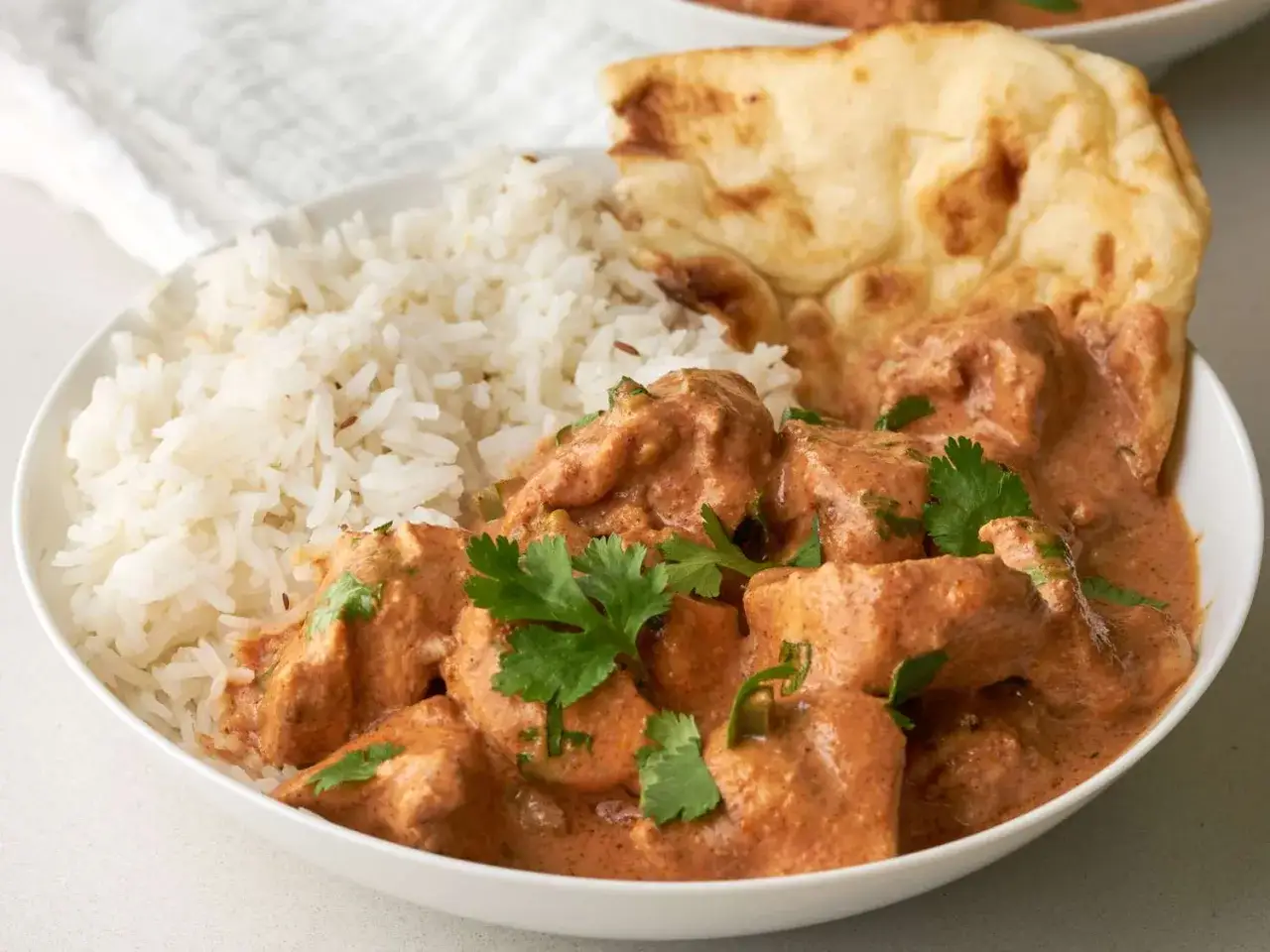 En sk&aring;l med kr&auml;mig chicken tikka masala, ris och naanbr&ouml;d. Garnerad med f&auml;rsk koriander.