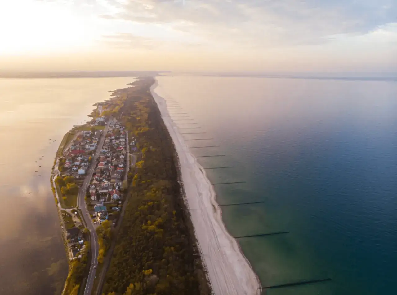Widok z lotu ptaka na plażę w Chałupach, z zabudowaniami po jednej stronie i morzem po drugiej.
