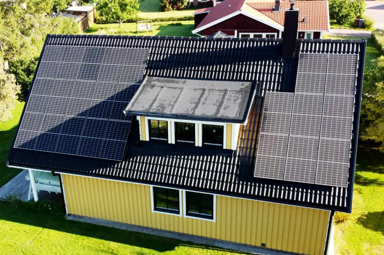 Gult hus med svart tak täckt av solpaneler. Ett modernt hem som fångar solens energi.