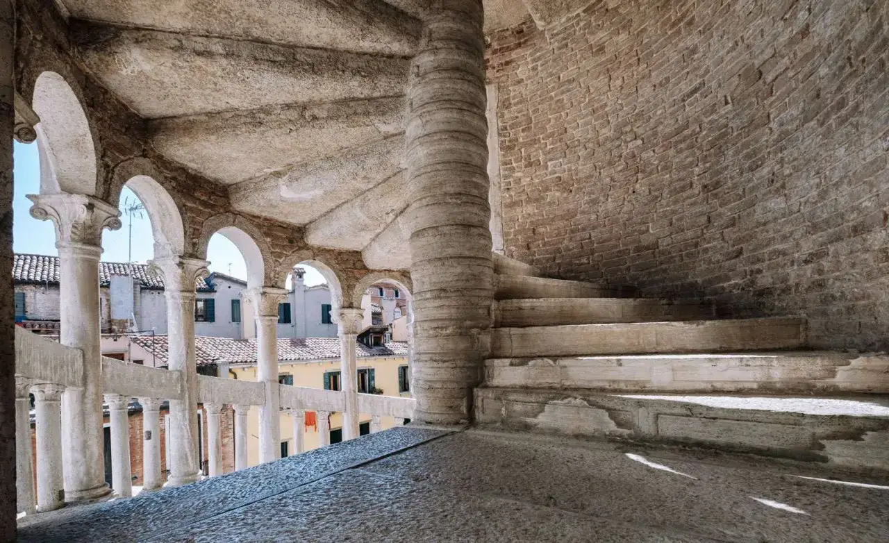 La scala Contarini del Bovolo, con i suoi gradini in pietra e il pilastro centrale a spirale, si affaccia su un panorama di tetti veneziani.