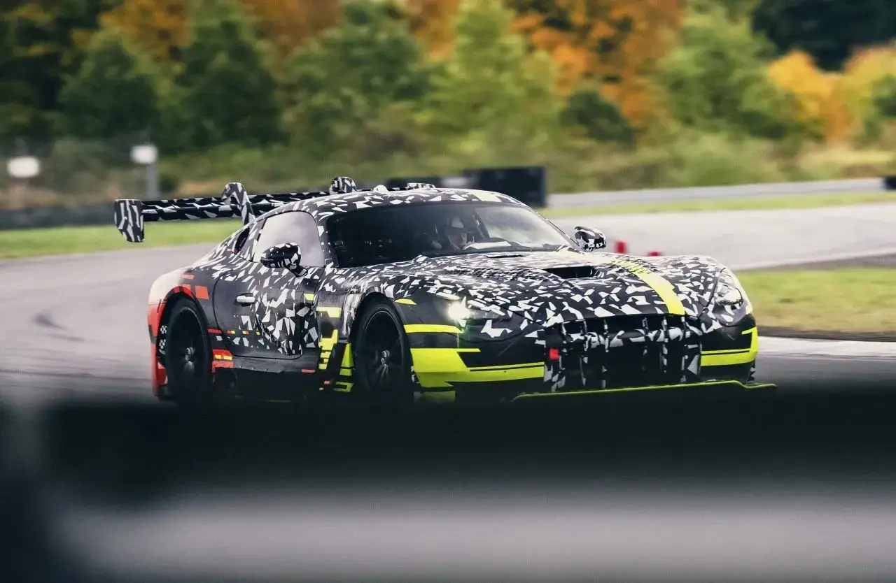 Zamaskowany Mercedes-AMG GT Black Series pędzi po torze wyścigowym, z jaskrawożółtymi akcentami i masywnym skrzydłem.