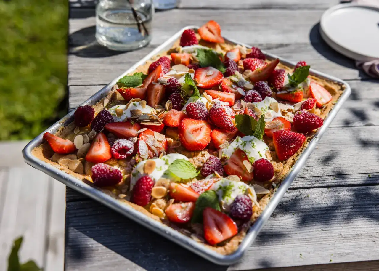 Enkel t&aring;rta med f&auml;rska jordgubbar, hallon, gr&auml;dde och mandelflagor p&aring; ett tr&auml;bord utomhus.