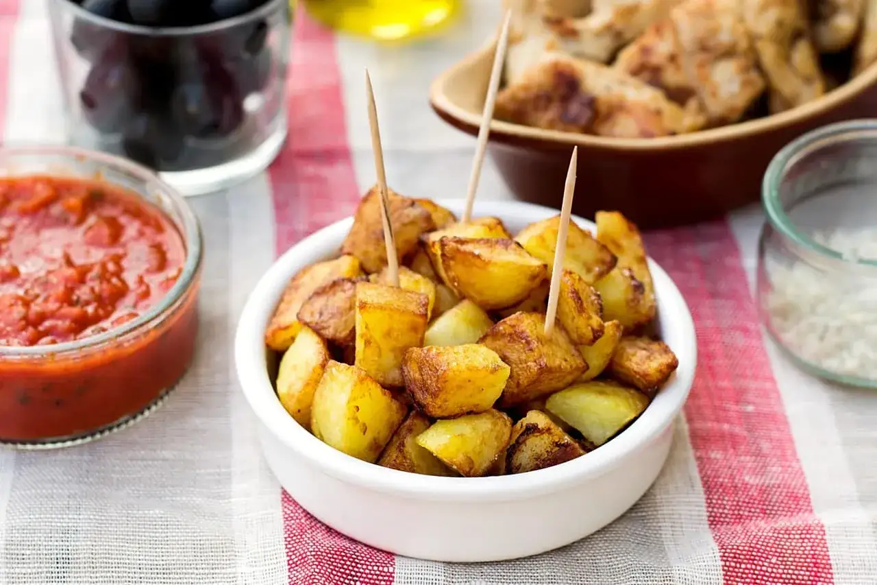 Patatas bravas dorées, servies avec une sauce piquante et des olives noires. Un délice pour les tapas !