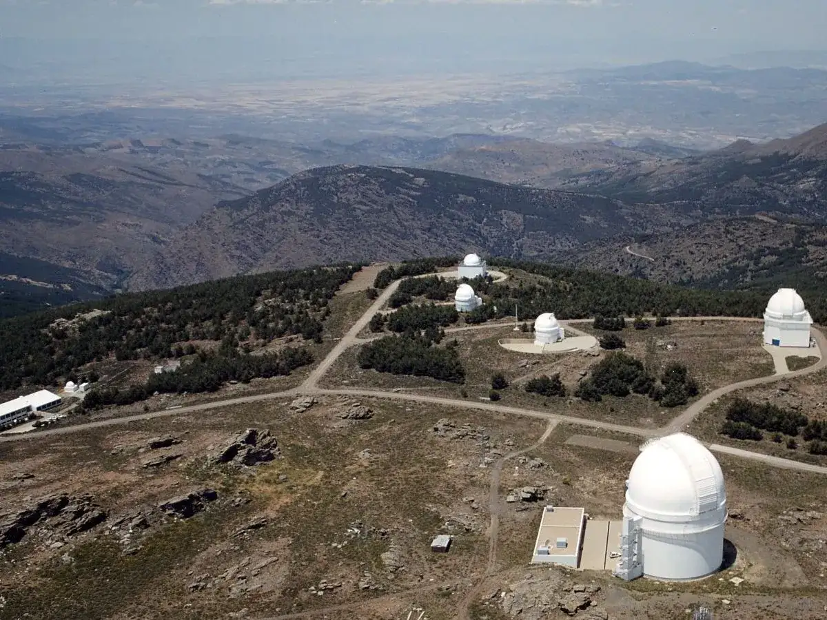 Observatorio astron&oacute;mico en el calar alto, con c&uacute;pulas blancas dispersas entre pinos y un paisaje monta&ntilde;oso al fondo.