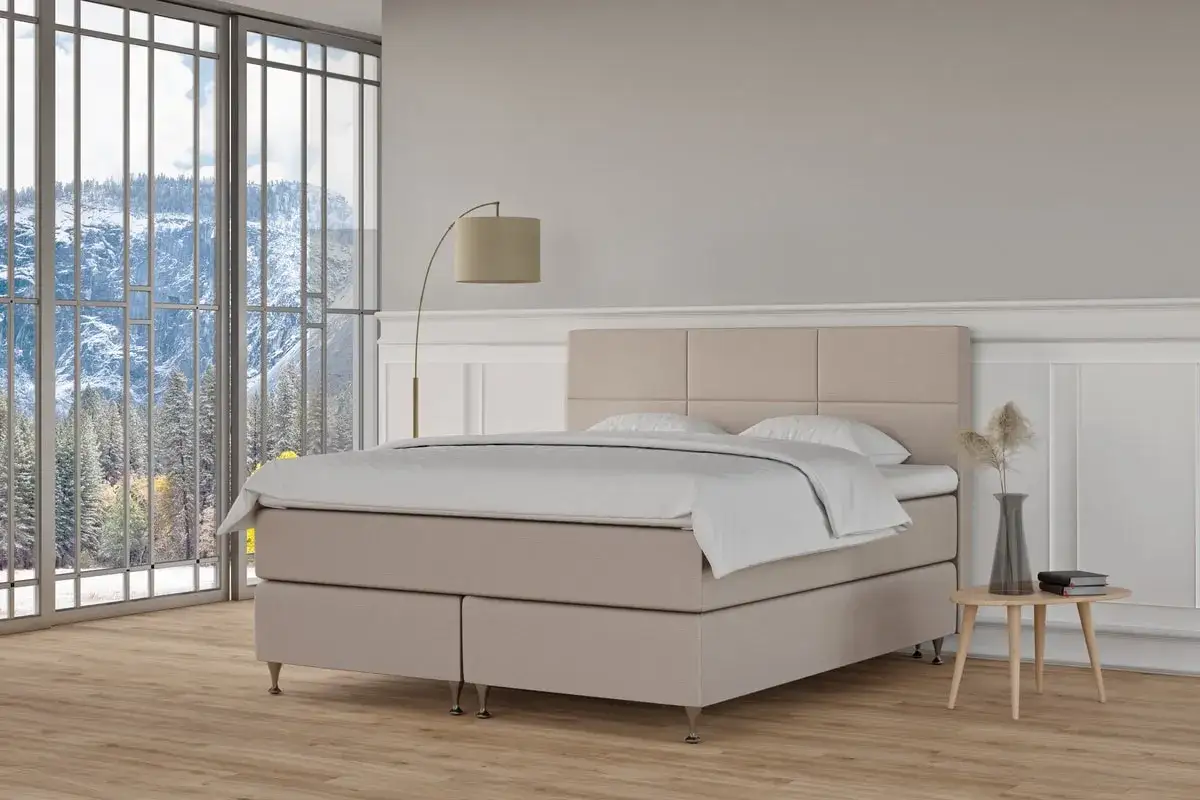 En bekväm säng 100x200 med en stilren beige klädsel och en mjuk kudde. Sov gott med utsikt över ett snöigt vinterlandskap.