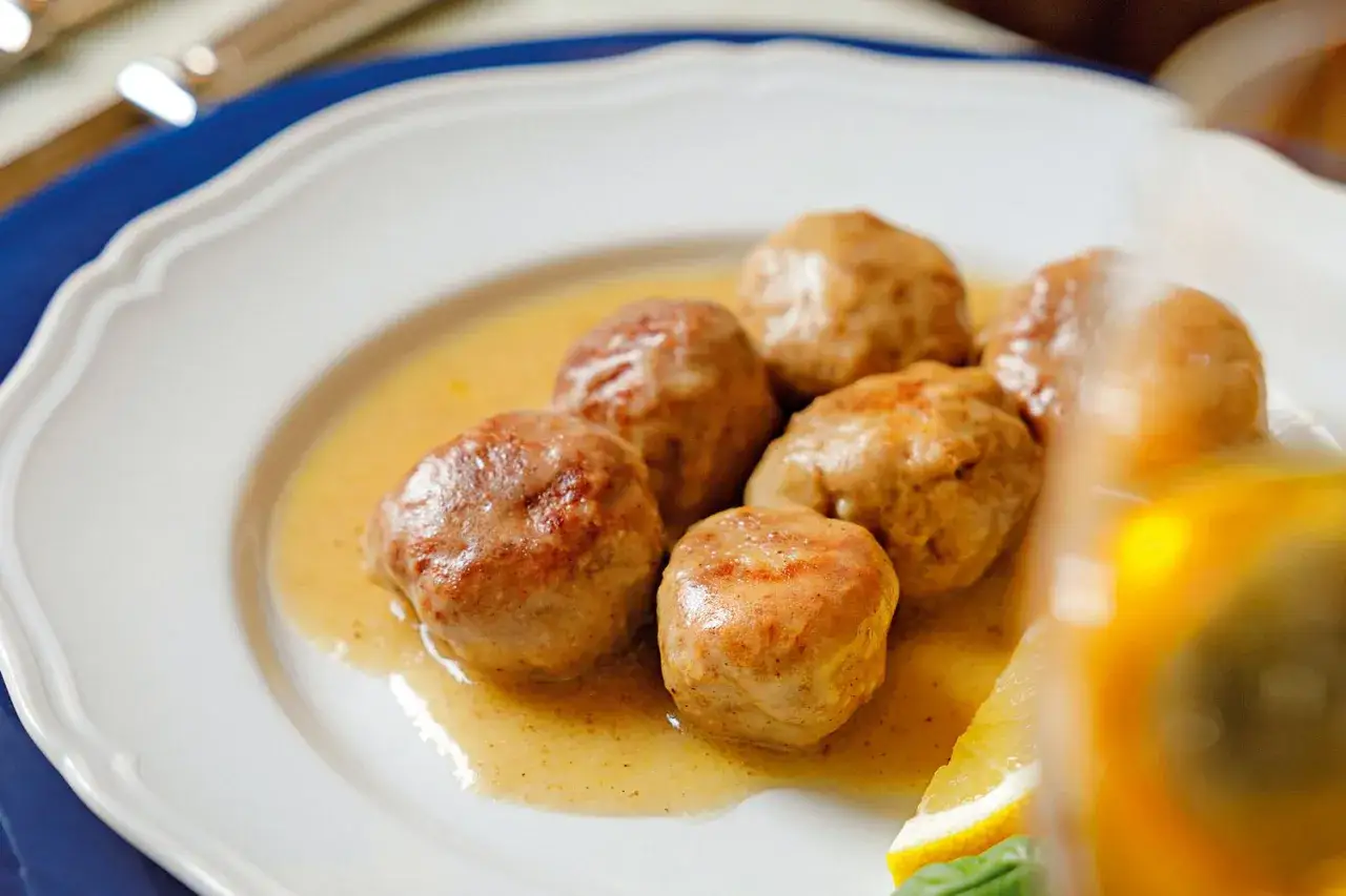 Polpette al limone succulente in salsa dorata, servite su un piatto bianco con una fetta di limone e basilico.