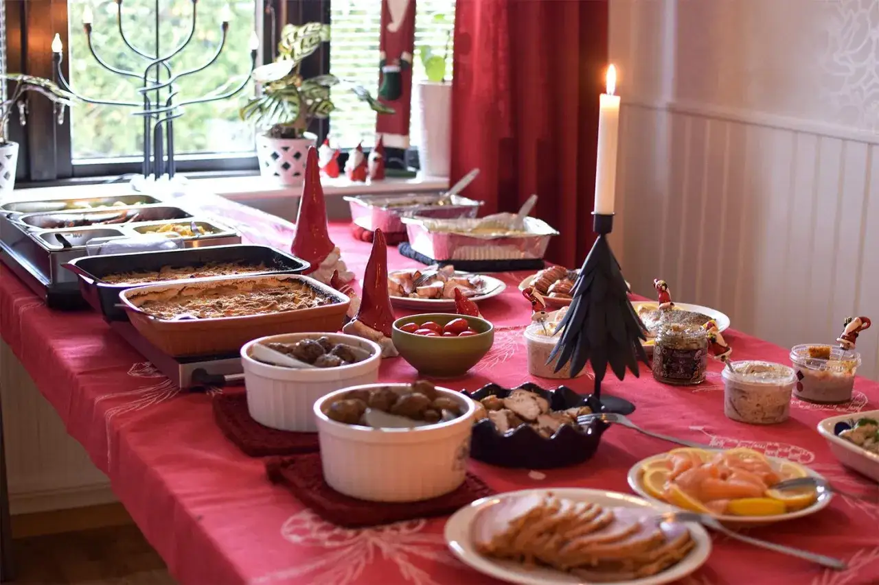 Julens historia på ett dukat bord med julmat, ljus och tomtar. En festlig buffé som bjuder in till gemenskap.